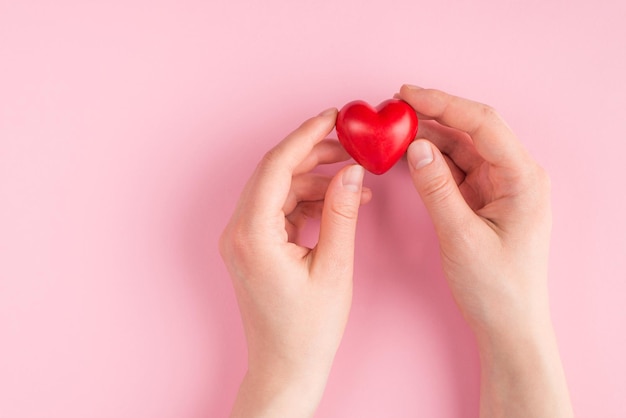 Top above overhead pov first person view photo of female hand holding a red heart isolated on pink pastel background with copyspace