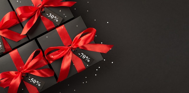 Top panoramic view photo of black gift boxes with red satin ribbon bow on isolated black background with copyspace