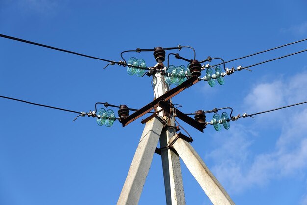 Top part of pillar of power supply line with wires and insulators under blue sky with white clouds