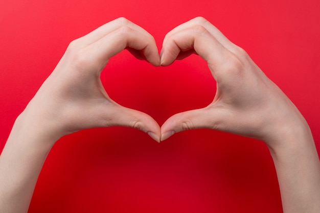 Photo top pov above overhead close up view photo of woman making heart with her hands isolated on red background