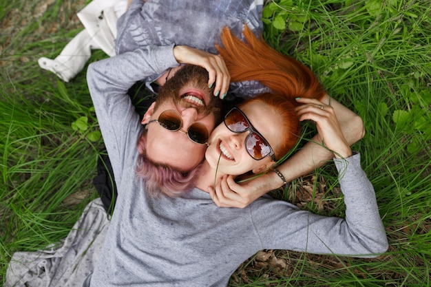 Top smiling people in a sunglasses, seated down on a green grass, looking at camera.