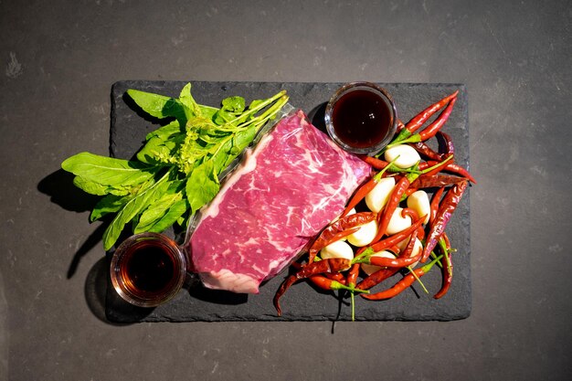 Top table flatlay of Raw Beef herb ingredients basil garlic chilli sauces on black slate plate for Thai cooking menu Stirfried beef basil Clipping Path