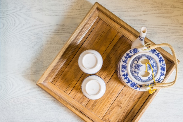 Top of traditional white cup of tea and teapot in wooden tray closeup on table