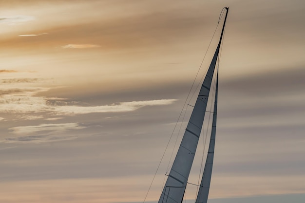 Top van mast van zeiljacht bij zonsondergang oranje hemel zeilregatta magische wolken hemel