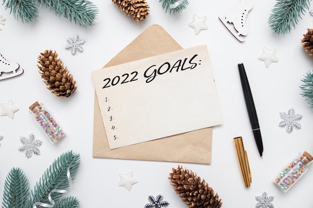 Top view of 2022 goals on sheet of paper and pen with envelope on table with winter decor