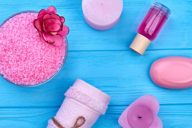 Top view accessories for bath and spa on blue wooden desk. Pink himalayan salt with soap, candle and perfume.