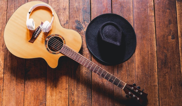 Top view acoustic guitars with earphones and hipster hats on\
old wooden backgroundcountry music