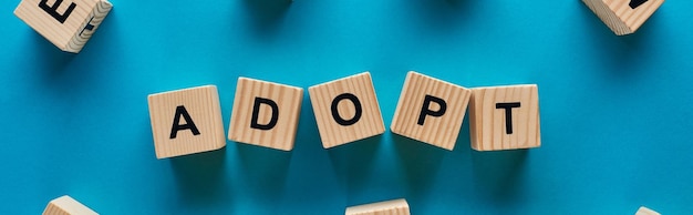 Top view of adopt word made of wooden cubes on blue background panoramic shot