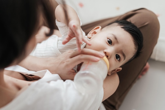 아기 병에서 마시는 귀여운 작은 아시아 아기 엄마가 아기 병으로 먹이는 귀여운 아들을 들고 있는 아기 개념 아기 건강 관리