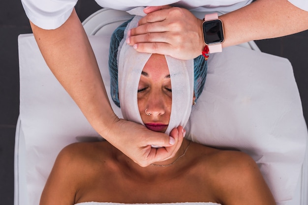 Top view of an adult woman receiving a skin care treatment with gauze by cosmetologist in the beauty salon.