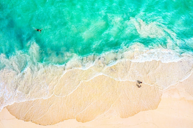 Top view aerial drone photo of ocean seashore with beautiful turquoise water, foam sea waves and people. Caribbean resort. Vacation travel background.