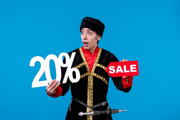 Top view of afraid young guy wearing traditional dress and holding percent writing sale icon on blue background