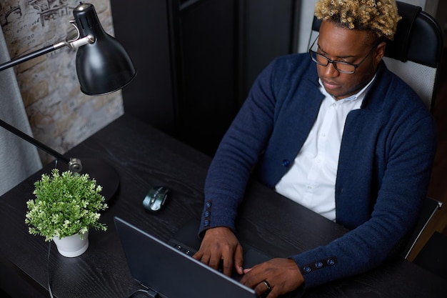 Top above view African employee working with laptop sitting at office desk