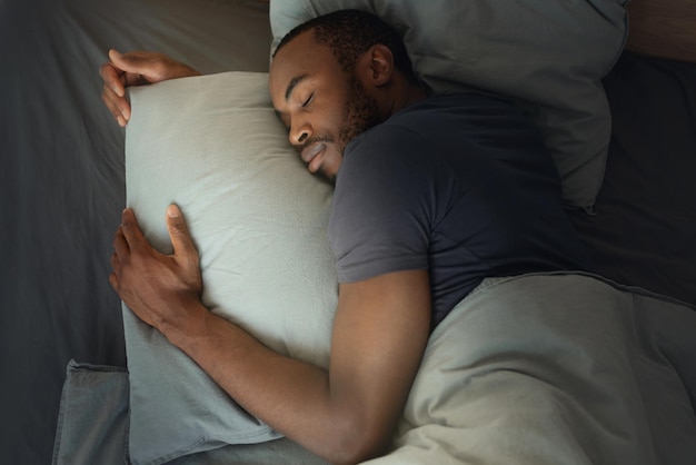 Foto vista dall'alto dell'uomo africano che dorme abbracciando il cuscino in camera da letto