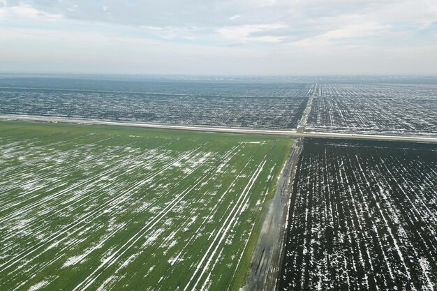 Top view of agricultural green and brown fields covered with snow.