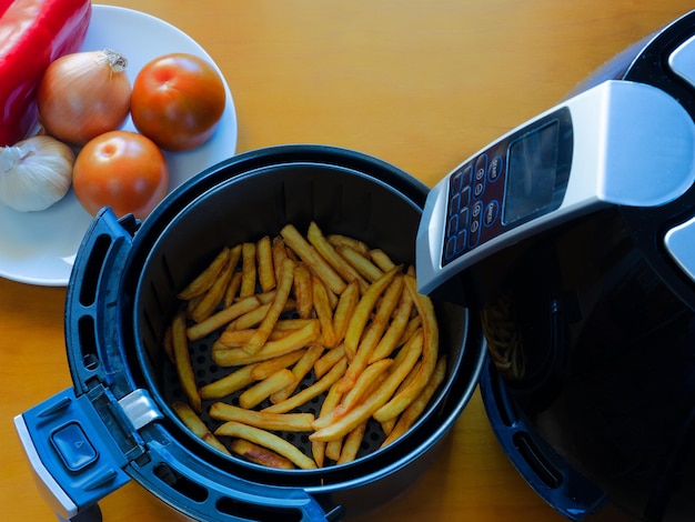 Top view of an air fryer on a table with french fries and vegetables Healthy food concept