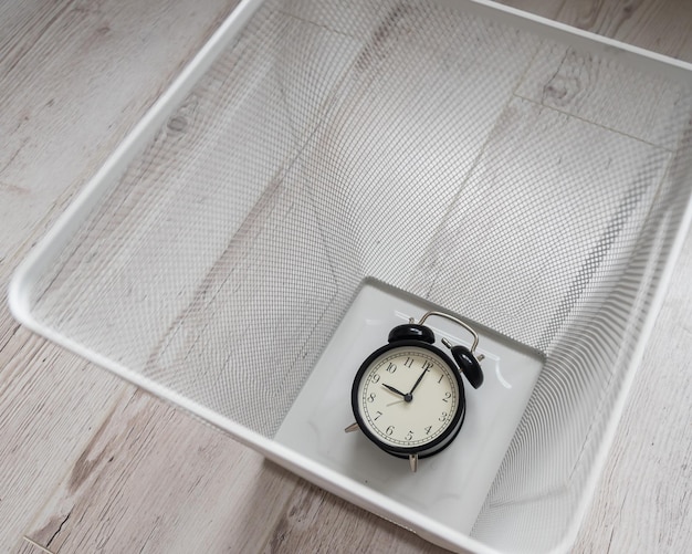 Top view of an alarm clock discarded in a white mesh metal trash bin The concept of wasted time