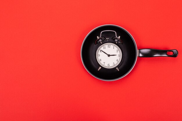 Top view of alarm Clock in pan isolated on red 