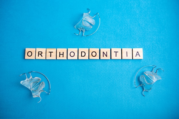 Photo top view of alphabet blocks with letters on a blue background. orthodontia - lettering.letters and orthodontic apparatus for the upper row of teeth