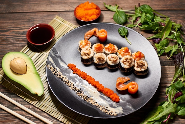 Top view of appetizing Japanese sushi rolls in big black plate serving with fish slices sauces caviar avocado salad