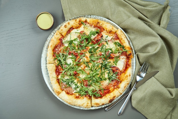 Top view on Appetizing pizza with prosciutto, arugula, tomatoes, parmesan and mozzarella on wooden table in a restaurant. Italian cuisine.