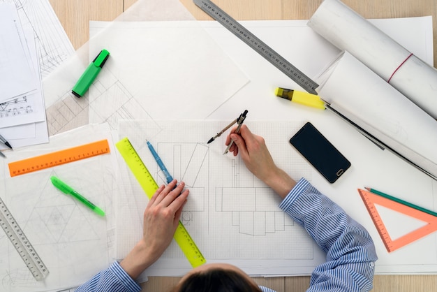 Top view of the architect's woman at work on the design of the building, on the table paper, rulers, pencils, compass, smartphone, twisted drawing