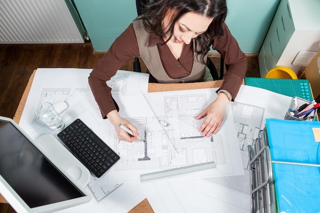 Photo over top view of architect working at her desk with blueprints in front of her. working on new projects. architecture and design