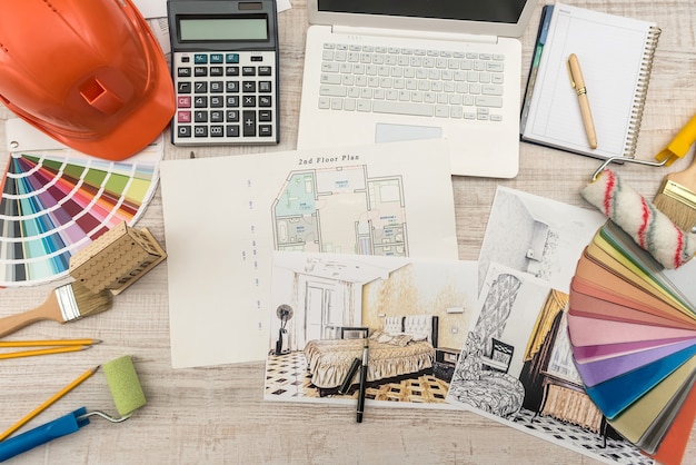 Vista dall'alto di architetti che disegnano casa moderna con materiale campione, elmetto protettivo, laptop sul tavolo creativo