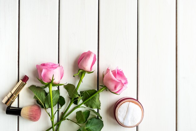 Disposizione di vista dall'alto con trucco, rose e copia-spazio su fondo di legno bianco