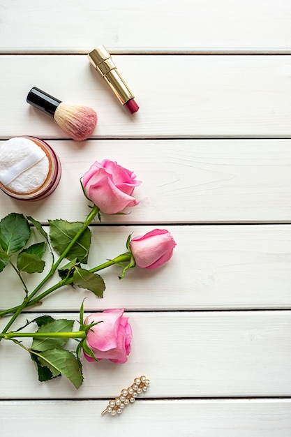 Disposizione di vista dall'alto con trucco, rose, tornante e copia-spazio su fondo di legno bianco. concetto di giorno, bellezza e femminilità della donna.