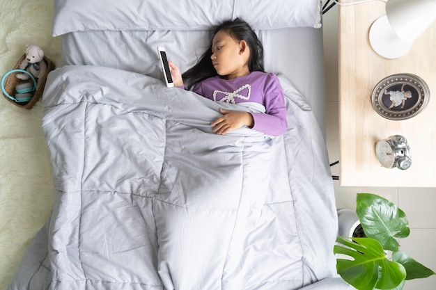 Top view Asian child little girl playing smartphone lying on the bed