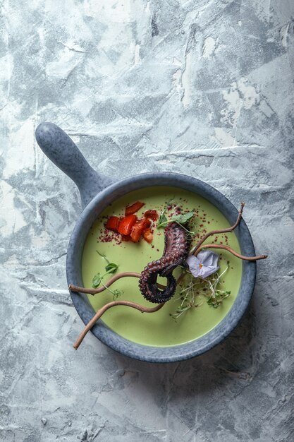 Zuppa di asparagi vista dall'alto con polpo in una ciotola grigia su un marmo grigio cemento