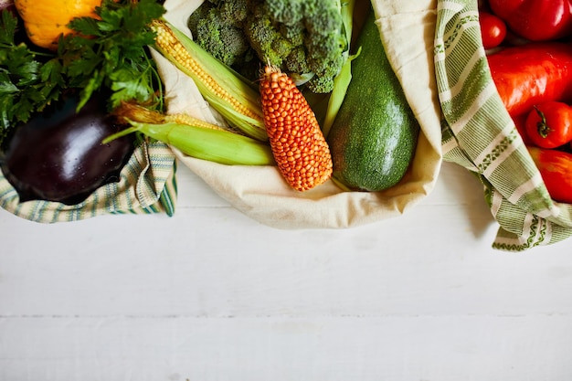 Top view assorted fresh vegetables in reusable cotton bags on table in the kitche in sunlight groceries in textile Zero waste bags Online grocery healthy shopping vegan food