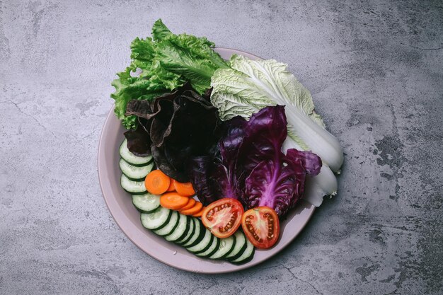 Top view of assortment fresh vegetables slices and green leaves on plate