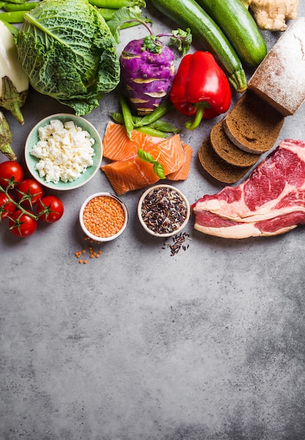 Top view of assortment of healthy balanced food: meat, fish, vegetables, bread, cereals, beans, stone background, space for text. Raw ingredients for cooking healthy meal, good for diet, clean eating