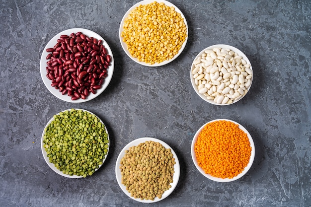 Top view of assortment of peas, lentils, beans and legumes over gray background.