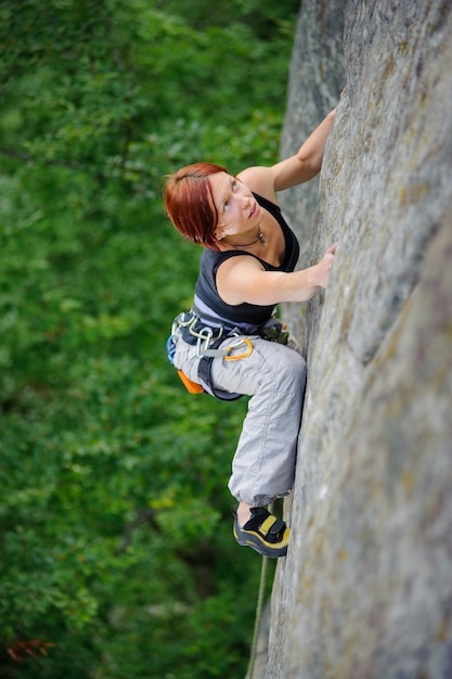 Top view of athletic woman climbing steep cliff wall