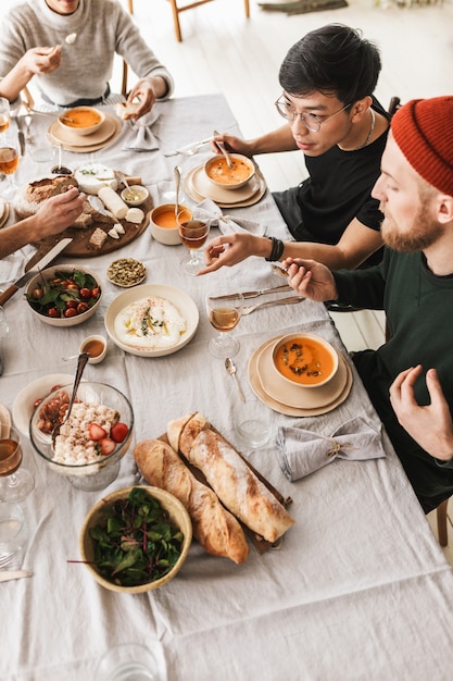 一緒に食べる食べ物でいっぱいのテーブルに座っている国際的な友人の魅力的なグループの上面図