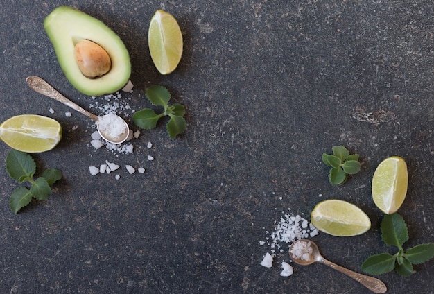 Top view of an avocado with slices of lime and kiwi on a black background with space for text