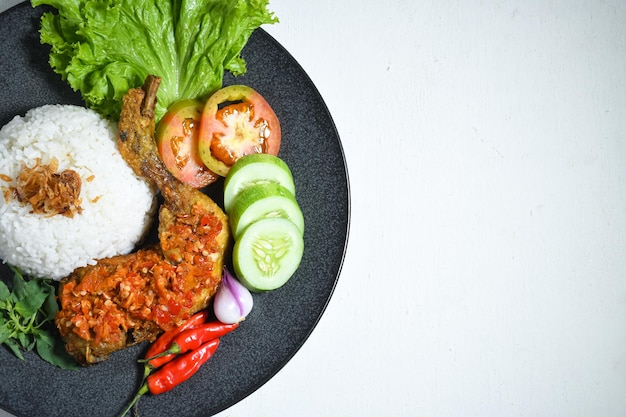 Top view Ayam geprek indonesian food with sambal hot chili sauce served rice on black plate