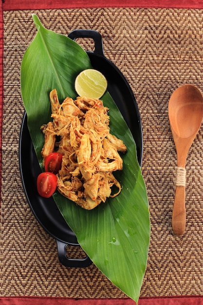 Vista dall'alto ayam suwir bumbu kuning (ayam sisit con spezie gialle) è una cucina balinese o indonesiana a base di pezzi di carne di pollo. servito su piatto ovale nero, copia spazio per testo o ricetta