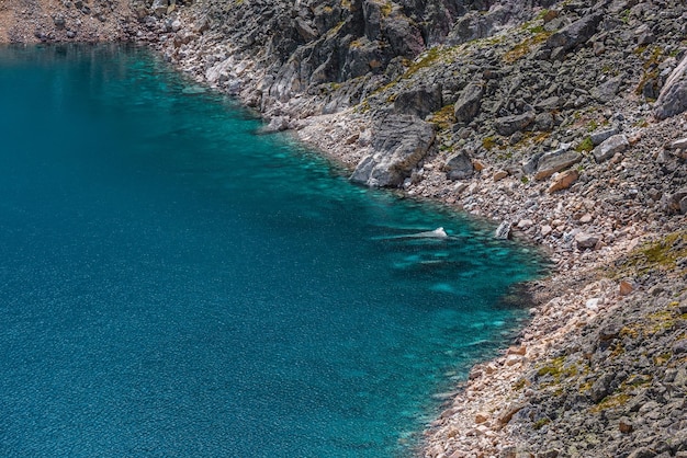 Top view to azure mountain lake with shiny cyan water edge among sunlit rocks beautiful alpine lake with stony bottom in transparent water in bright sun nature background of blue lake in sunlight