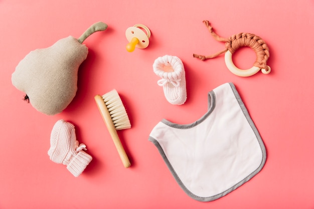 Photo top view of baby's bib; pacifier; sock; brush; stuffed pear and toy on peach background