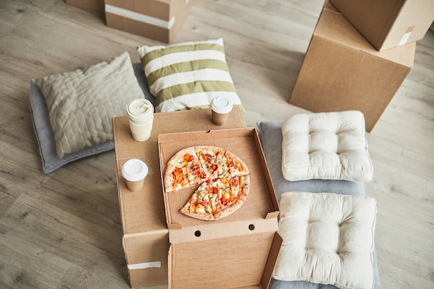 Immagine di sfondo vista dall'alto della pizza su scatola di cartone come tavolo improvvisato nella stanza vuota mentre la fami...