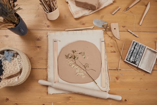 Фоновое изображение вида сверху необработанной керамики отпечатка растения на деревянном столе с инструментами в гончарной мастерской, копией пространства