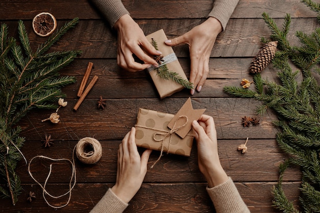 Top view background with two unrecognizable young women wrapping christmas presents at wooden table ...