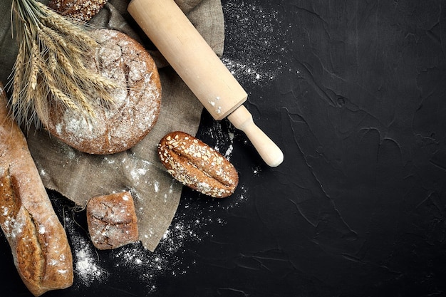 Top view of baguette baked bread flour and wheat spikes composition with wheat flour sprinkled around on a dark background