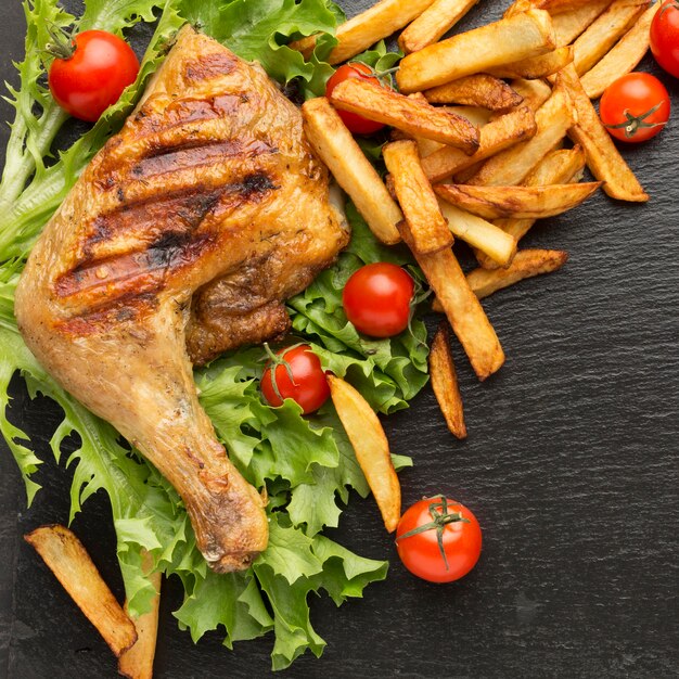 Vista dall'alto di pollo al forno e pomodori con patatine fritte