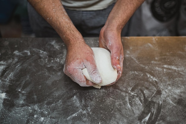 Top view of baker hands shaping bread dough at kitchen of bakery