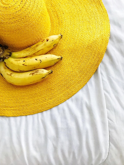 Top view of bananas placed on a yellow beach hat on a white bed
